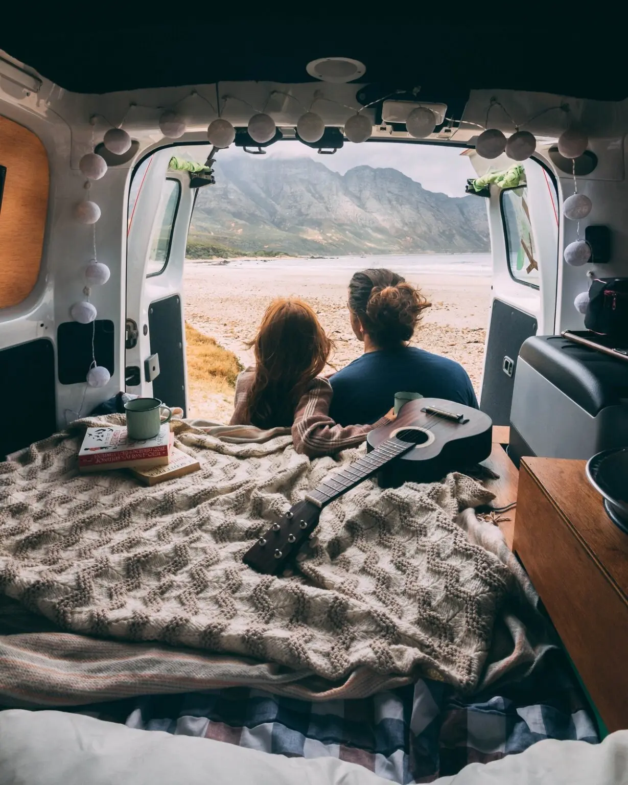 Zwei Personen genießen den Blick auf die Berge vom Inneren ihres Kastenwagens aus – perfekter Moment mit einem Ford Transit Custom für Campingfreunde.